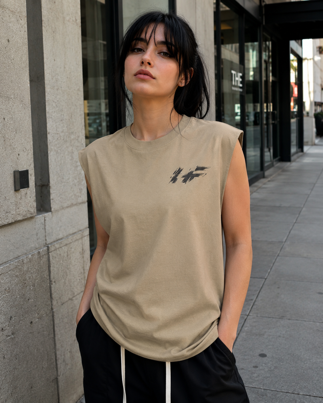 Woman wearing a beige sleeveless shirt with a HF logo on a city street.